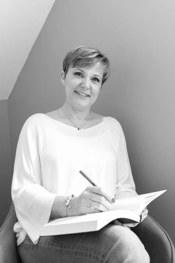 Photo représentant Véronique robillard assise sur un fauteuil en train d'écrire stylo à la main